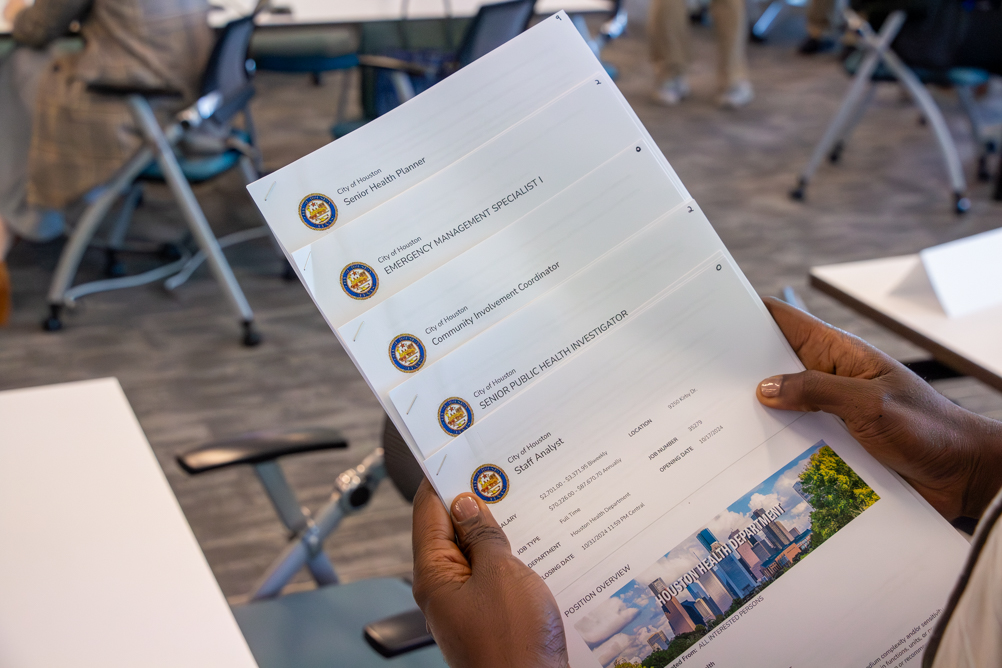 Close-up of hands holding printed City of Houston job listings, including public health and emergency management roles, at the career mixer.