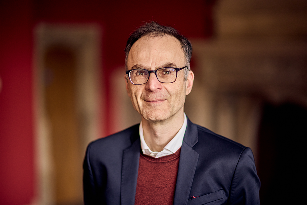 Professor Seena Fazel wearing glasses and a navy blazer against a softly blurred indoor background.