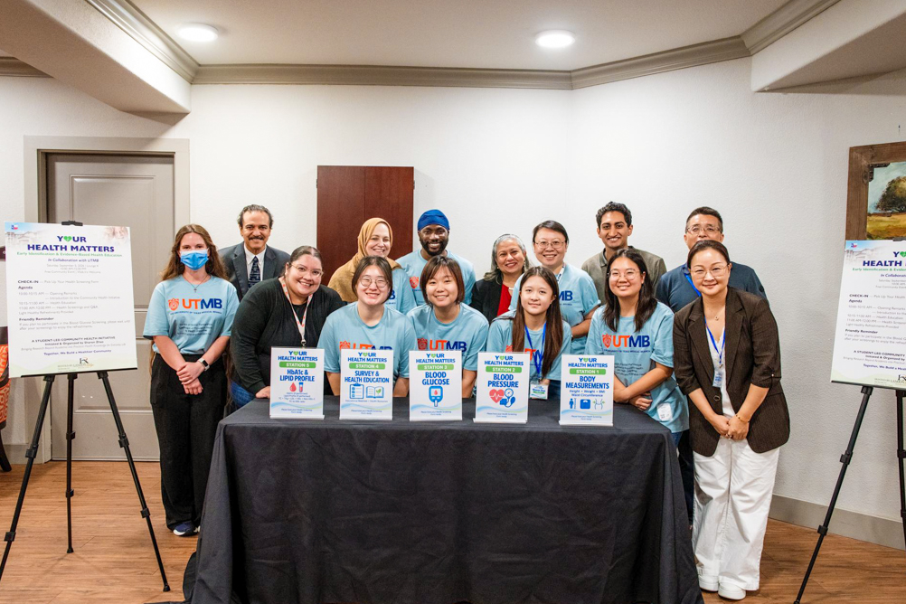The outreach team stands behind a UTMB Health table displaying stations for health education and screenings at Landon Ridge in Sugar Land.