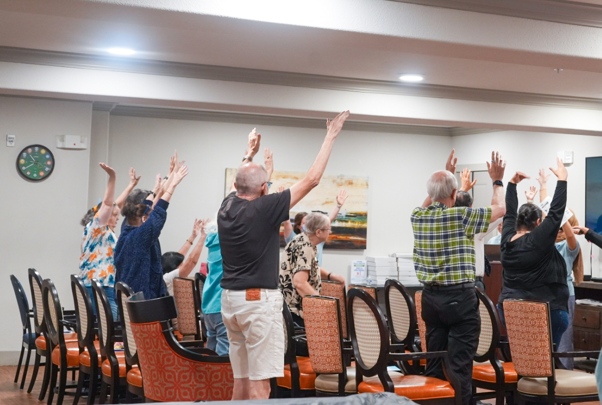 Landon Ridge residents raise their arms together during a guided stretching activity in a common room.