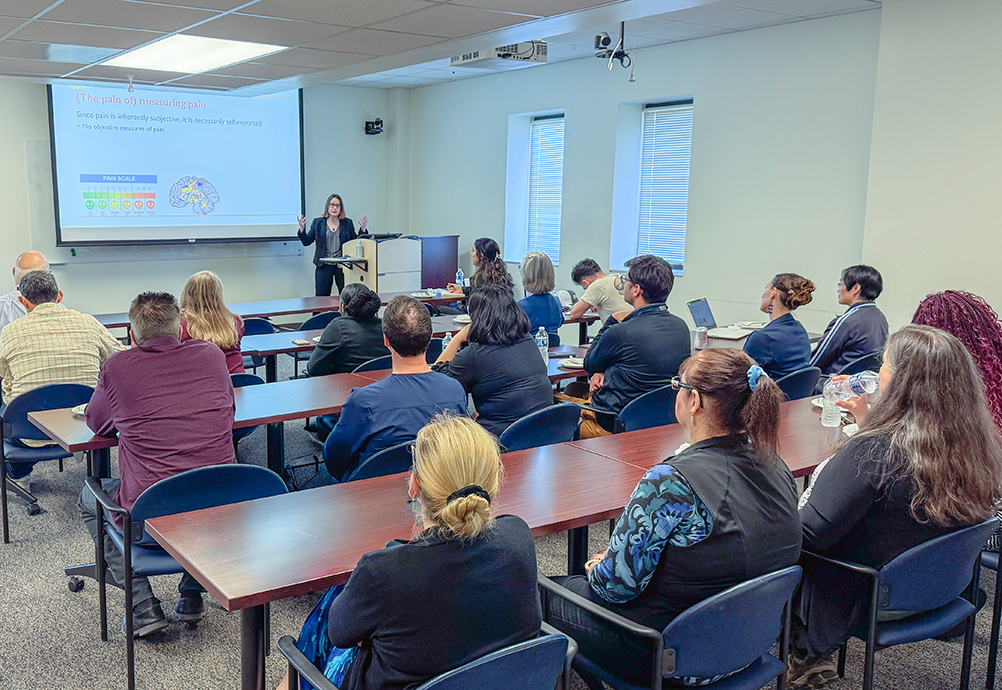 Anna Zajacova speaks to a classroom of attendees during a special lecture at UTMB, standing at the front of the room beside a projected slide about measuring pain.