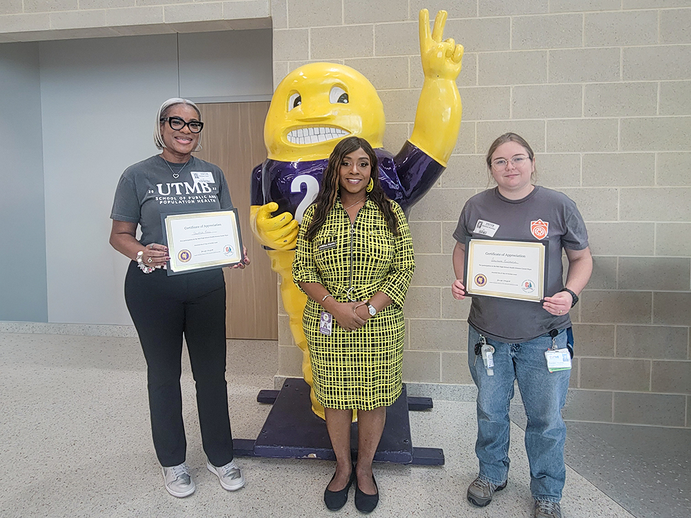 Christina Ross, Jamika Wilson-Harris and Anastasia Kuzmina stand in front of the Ball High School mascot, with Ross and Kuzmina holding certificates.