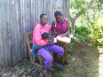 Two adults sit with a child on a chair outdoors.