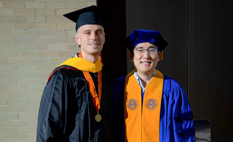 Faculty member and graduate pose together in academic regalia during a commencement ceremony.