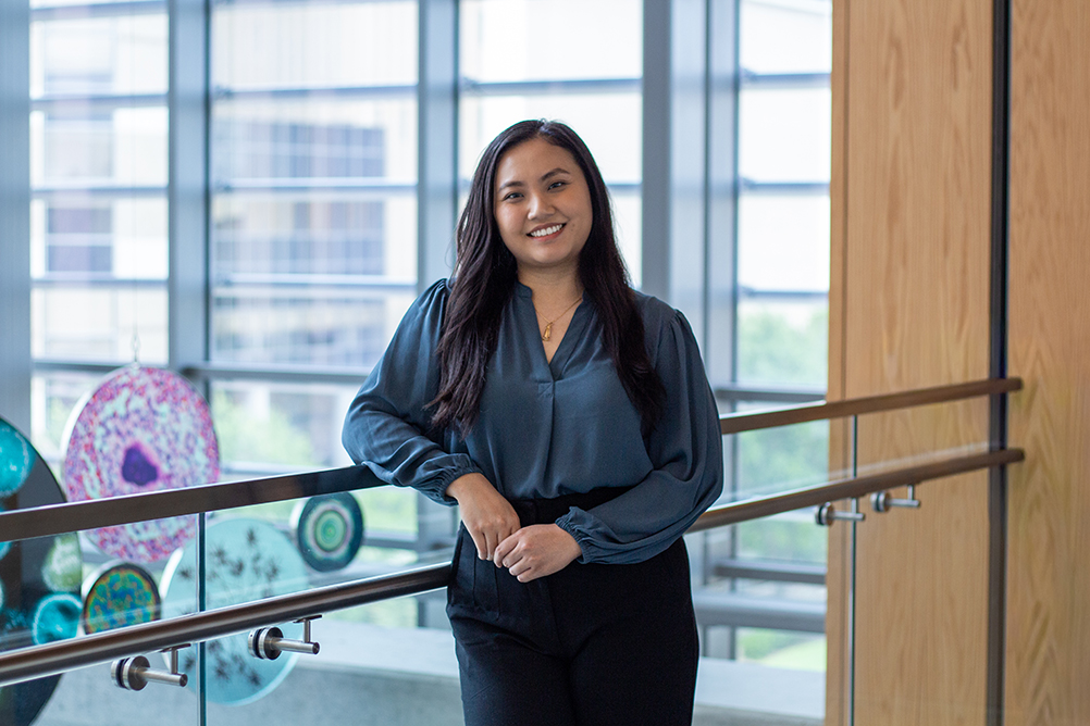 Anh smiles for a portrait inside a UTMB building, standing near a railing with large windows in the background.