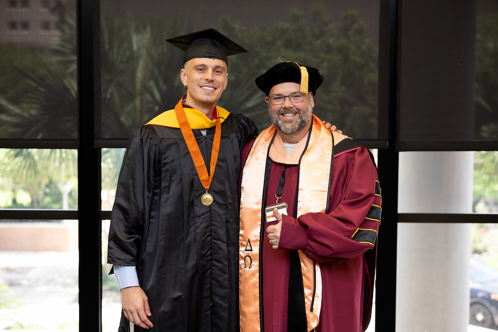 Griffin Baillargeon poses in graduation regalia with Dr. John Prochaska after the UTMB School of Public and Population Health commencement ceremony.