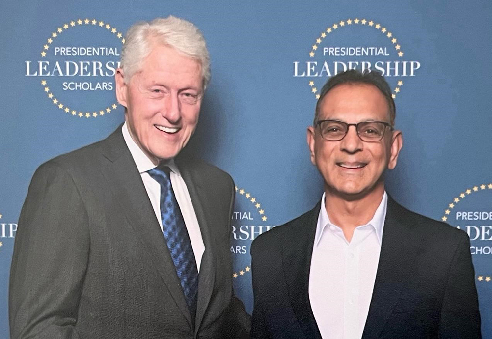 Dr. Suresh Bhavnani shaking hands with President Bill Clinton in front of a Presidential Leadership Scholars backdrop.