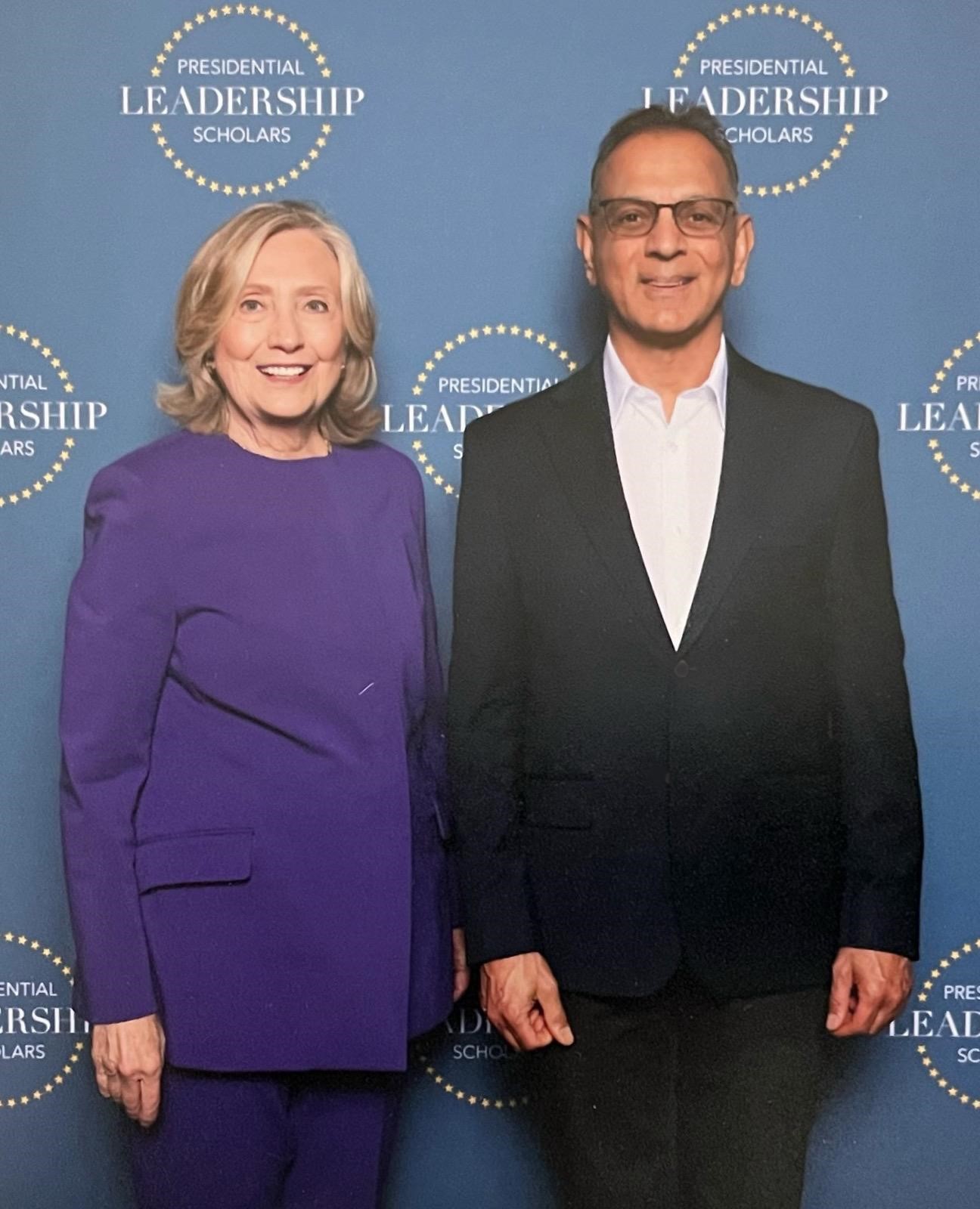 Dr. Suresh Bhavnani standing with Secretary Hillary Clinton in front of a Presidential Leadership Scholars backdrop.