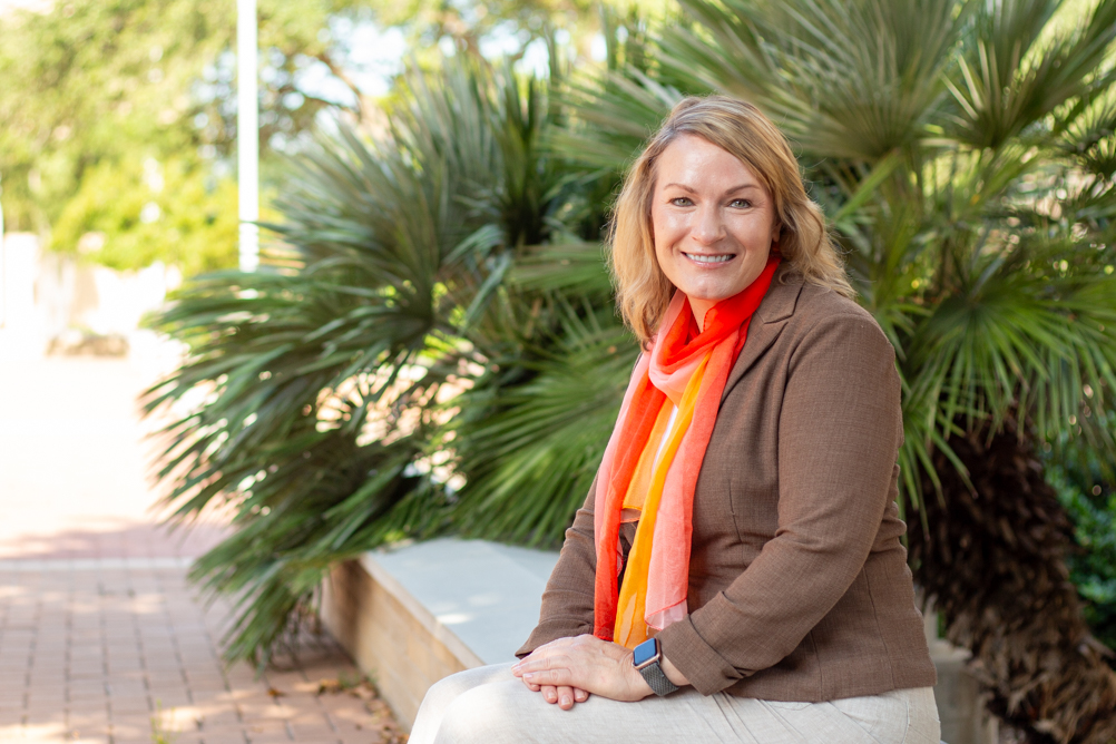 Dr. Cara Pennel smiles outdoors beside palm plants.