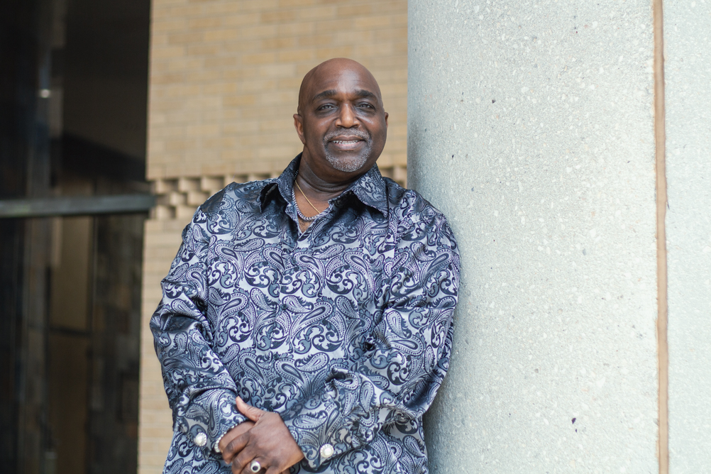 Headshot of John Cooks smiling beside a concrete column outside a campus building.
