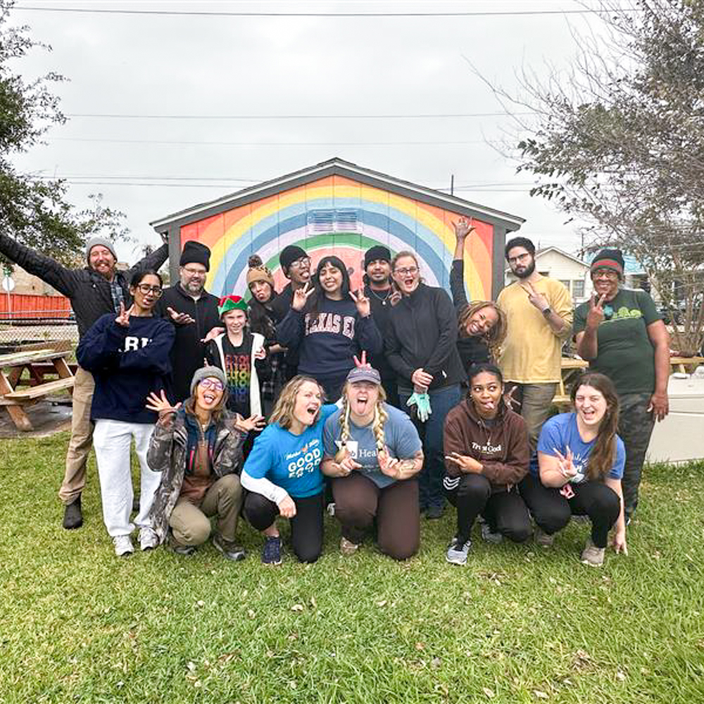 Group of volunteers from SPPH, Groundswell, and the community posing outside in front of a mural at an elementary school garden