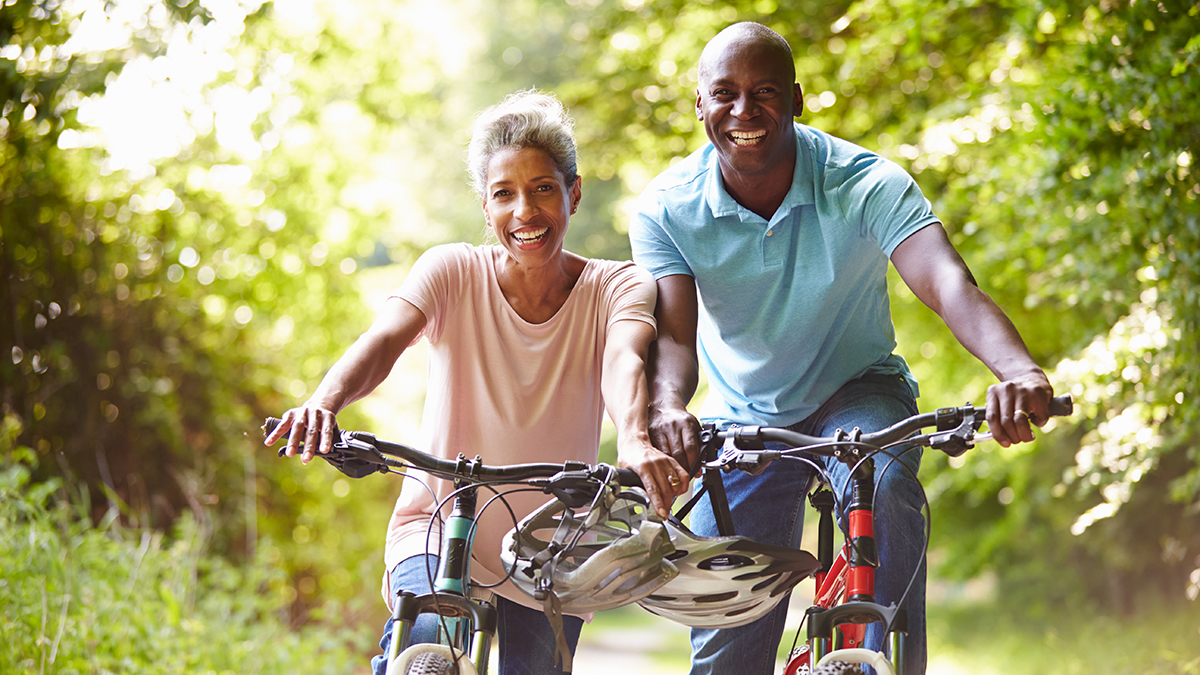A senior woman and man are riding bicycles together and smiling
