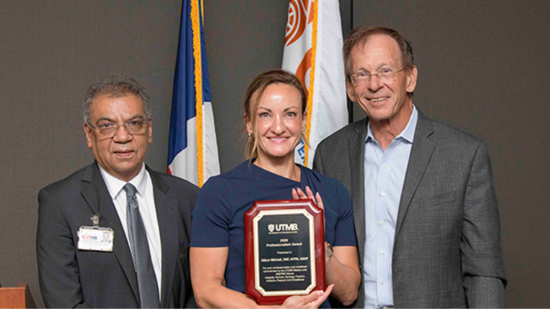 Allison Mitchell, center, holds a plaque for her Professionalism Award. Dr. Anish Bhardwaj and Dr. Tom Blackwell stand on each side of her.