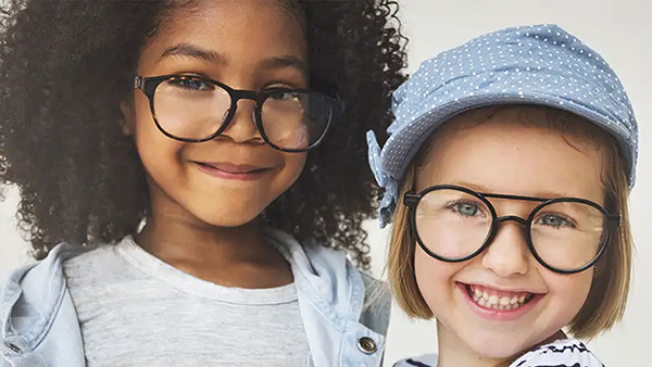Two young girls wearing glasses are looking at the camera and smiling.