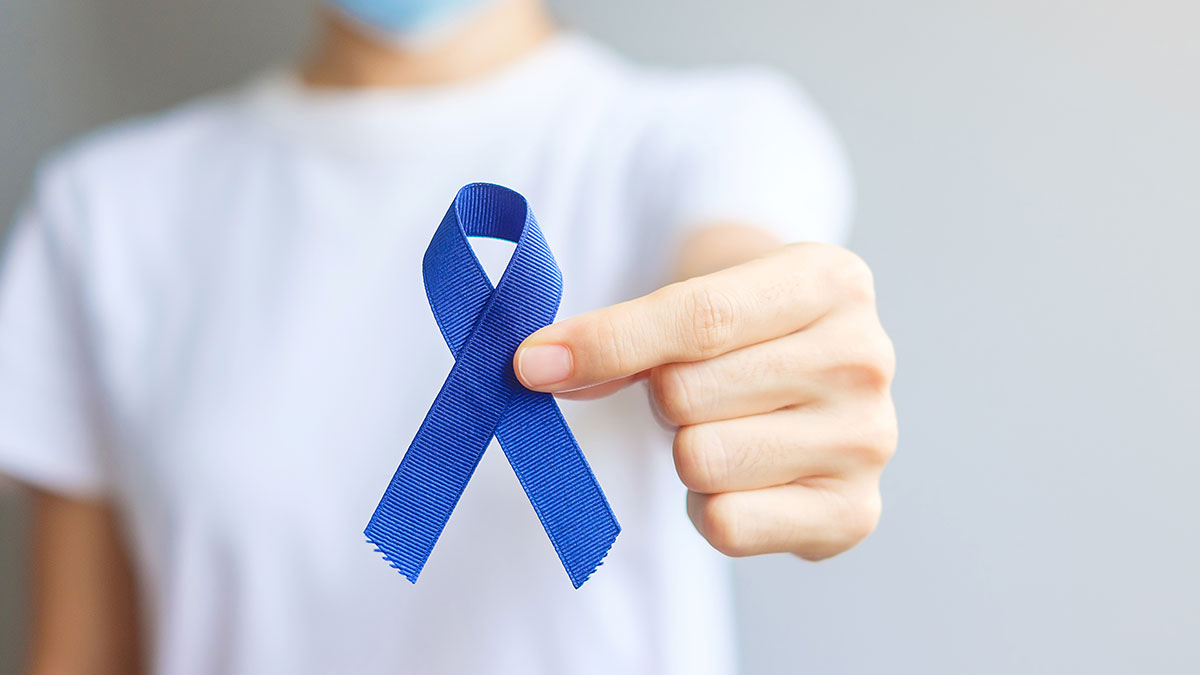 A blue ribbon is held close to the camera; the person holding is wearing a white shirt and is out of focus.