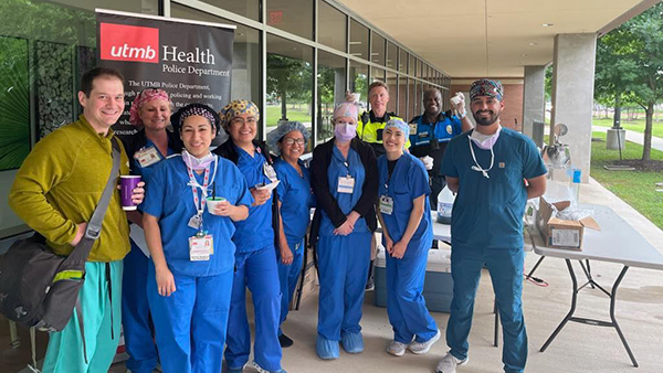 A group of health care employees in scrubs pose outside the hospital