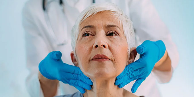 A clinician's gloved hands feel the sides of a woman's neck as part of a cancer screening
