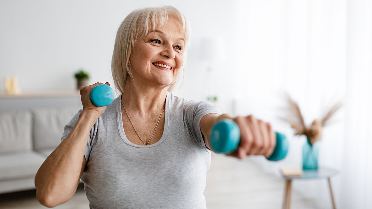 A woman with white hair is working out with dumbbells and smiling