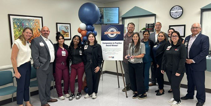 Clinic staff and leaders pose with balloons and a sign stating "Compassion in Practice Award Winner"