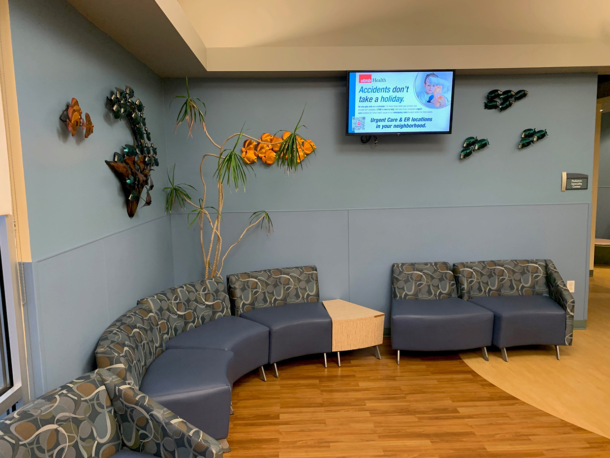 Photo of a corner waiting area with blue walls, fish decorations on the walls, a blue curved sofa and a TV screen mounted on one wall.