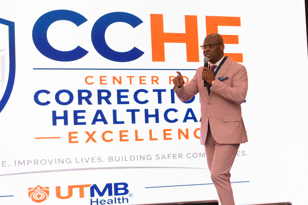 Olugbenga Ojo speaks onstage in front of the Center for Correctional Healthcare Excellence logo.