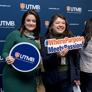Logo Launch Employees Two UTMB employees posing for a picture holding up signs with the new logo and stogan