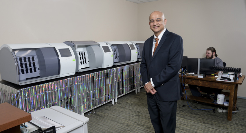 A man in a dark suit stands in a room lined with image scanning equipment.