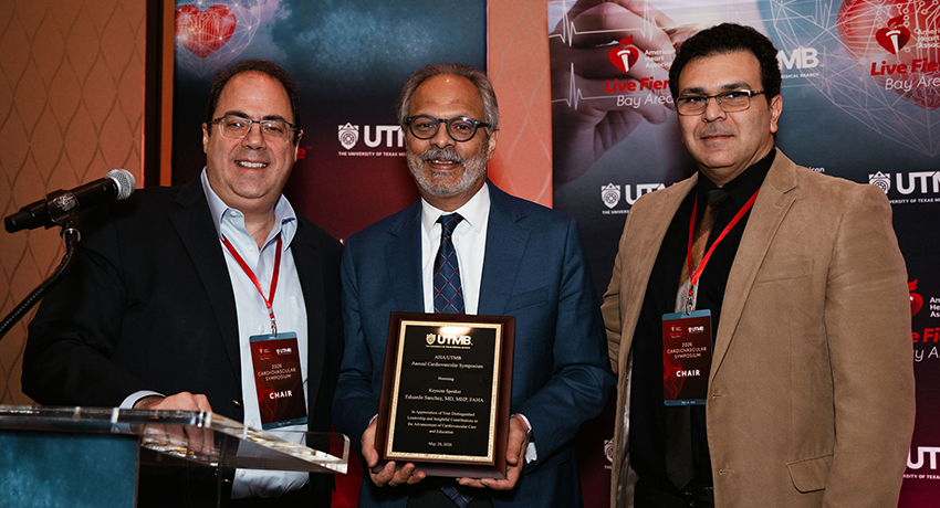 Two men wearing conference badges pose with a third man who is holding an appreciation plaque.