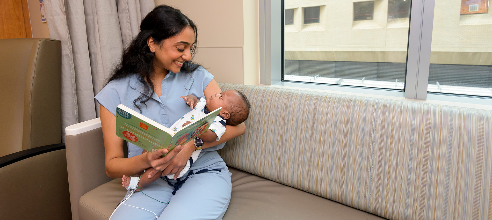 A volunteer and the infant in her arms in the NICU make eye contact during a reading session.