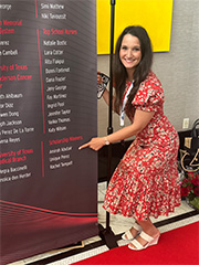 Woman standing in front of a black and red sign pointing to her name. 