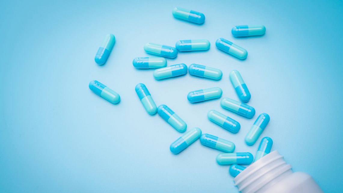 Several blue and white capsules scattered on a light blue surface next to an open medication bottle