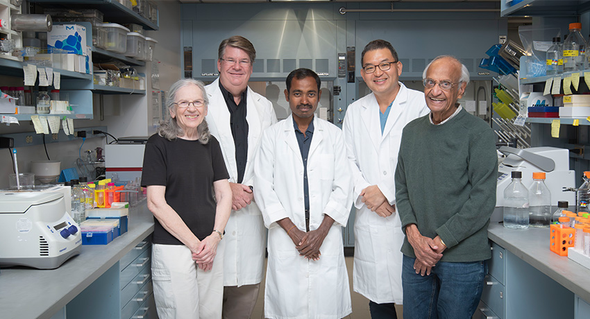 Five people standing in a lab setting at The University of Texas Medical Branch with three wearing white coats.