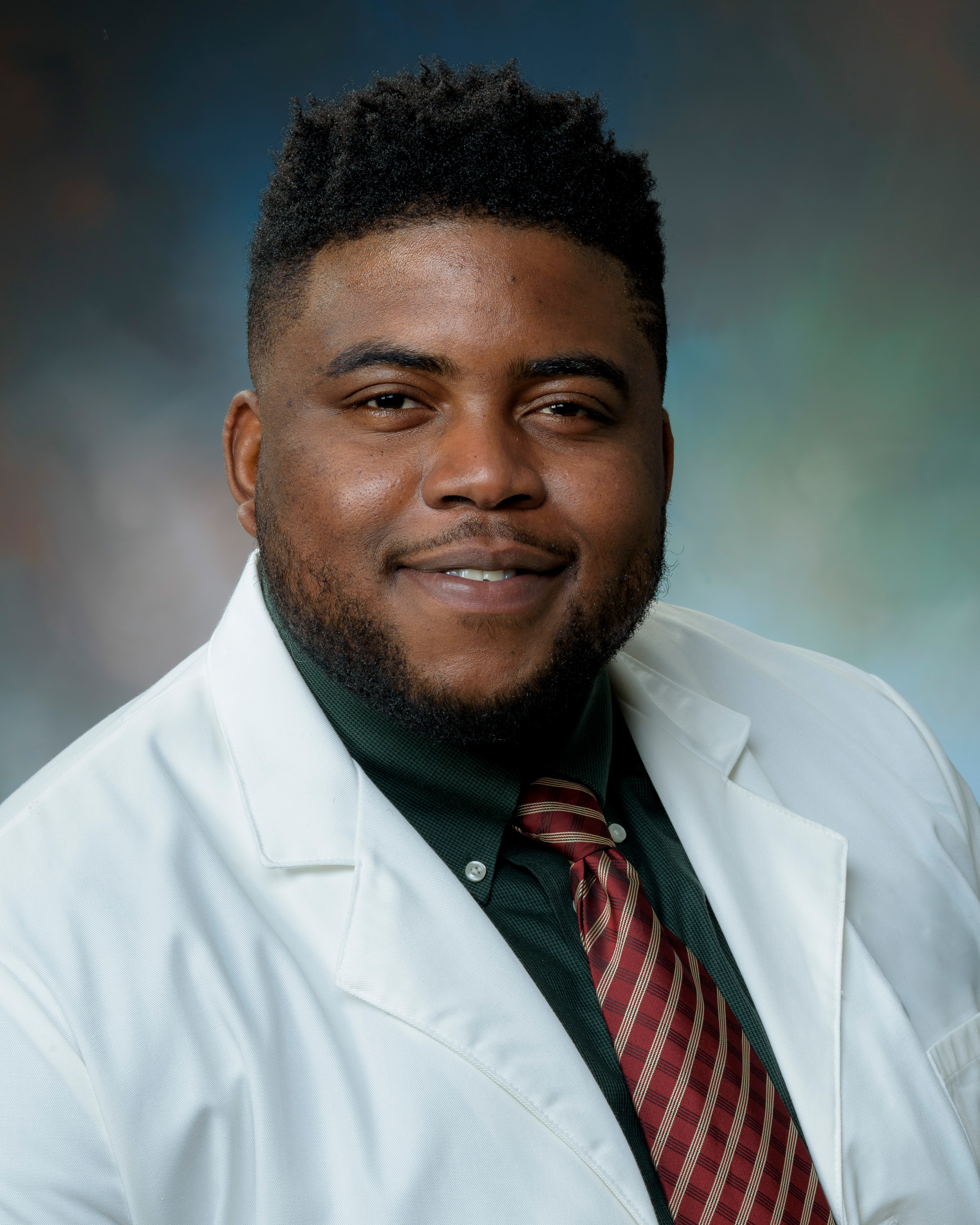 Dr. Ben-Okoli Studio headshot of an Dr. Ben-Okoli wearing a white lab coat, collared shirt, and patterned tie, looking at the camera against a blue‑green gradient background.