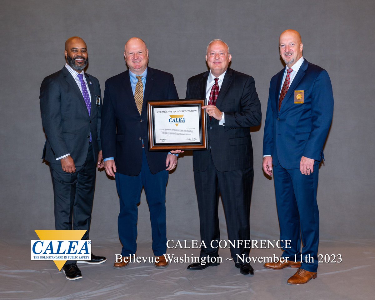 Four UTMB men wearing suits and ties display framed CALEA accreditation
