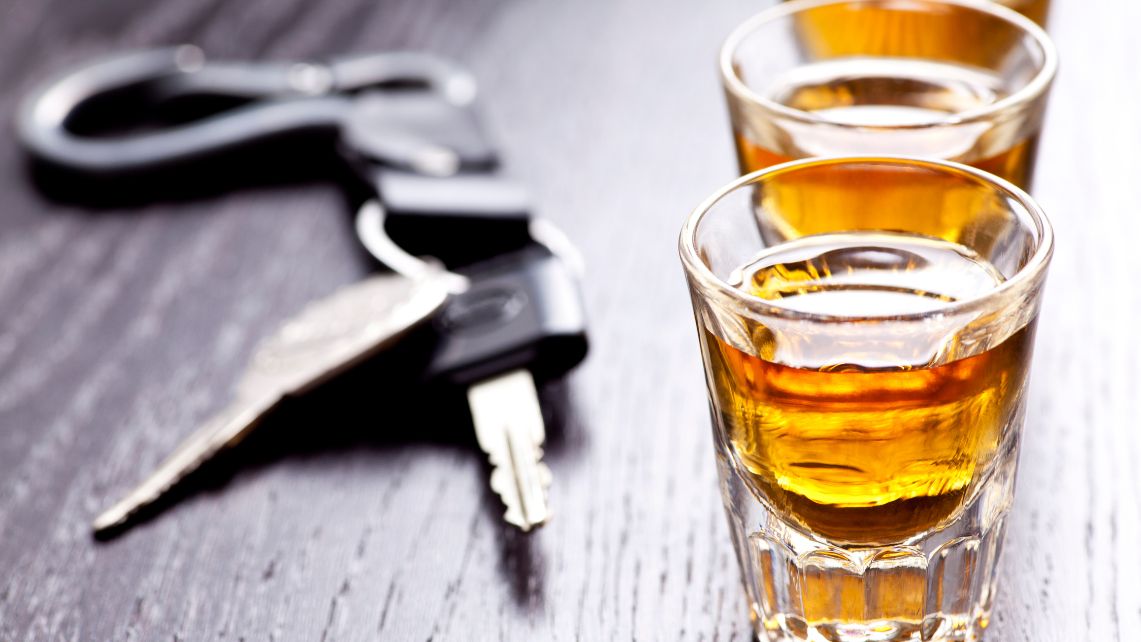 A set of car keys next to two shot glasses with amber colored liquor