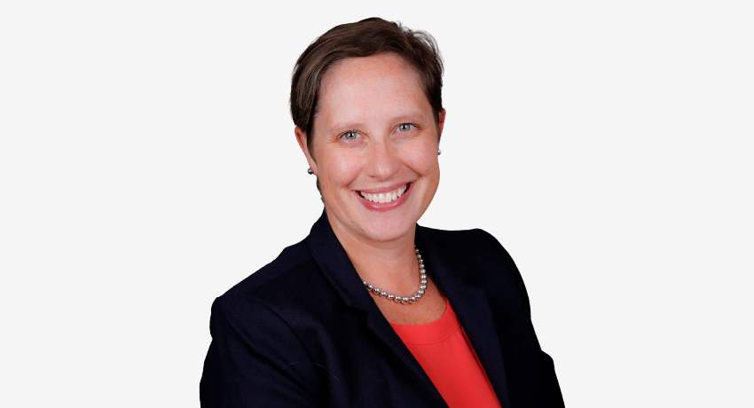 Dr. Cora Rabe, wearing a black jacket over a red shirt, smiles in a professional headshot.