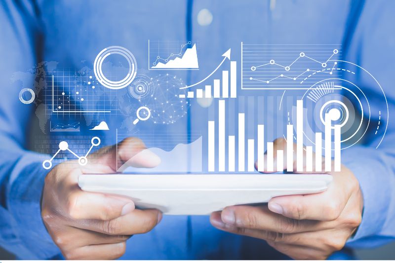 An image of a person wearing a blue shirt holding a tablet with projections of different data