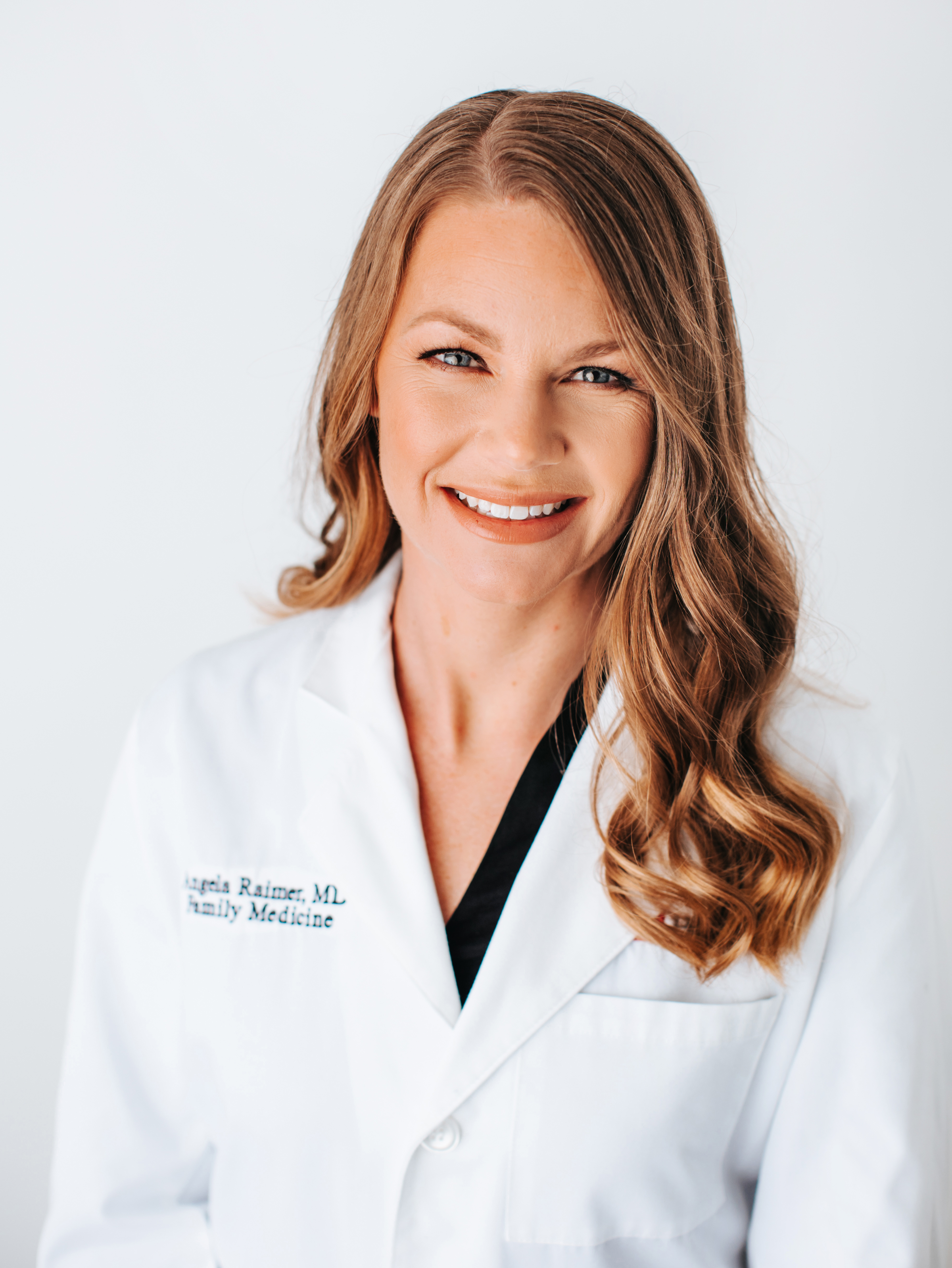 Clinician wearing a white lab coat against a light background, with the face intentionally obscured by a solid rectangle.
