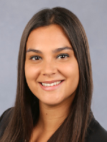 Person with long, straight dark hair wearing a dark blazer against a plain gray background.