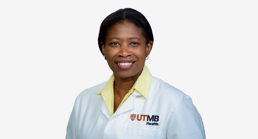 Studio headshot of a woman facing the camera, wearing a white lab coat with a UTMB Health logo over a light gray background.