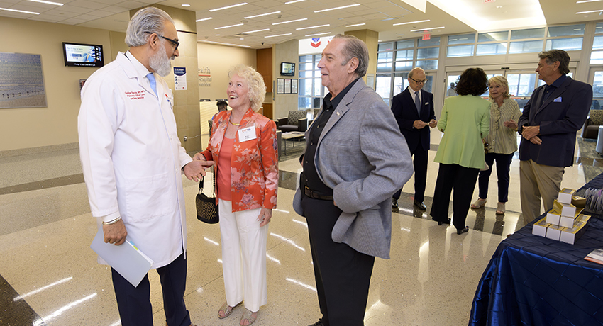 Dr. Gulshan Sharma, wearing a white UTMB coat speaks with a man an a woman dressed up to celebrate the hospital's anniversary.