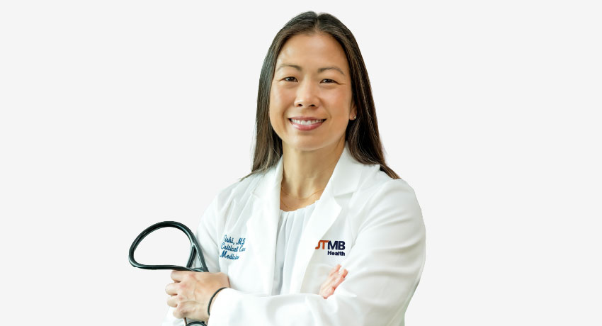 Person in a white UTMB Health lab coat stands with arms crossed, holding a stethoscope. The UTMB Health logo is visible on the coat.