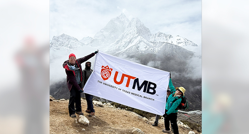 A snow-covered mountain peak rises above a layer of clouds, with sharp ridgelines visible against a clear blue sky, including 3 people holding a UTMB flag.