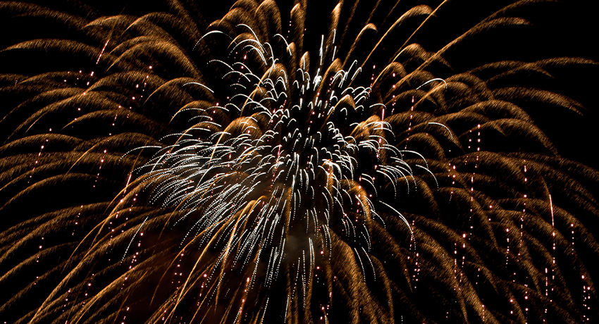 Large golden fireworks burst spreading across a dark night sky, with bright streaks radiating outward and smaller sparkles trailing below.