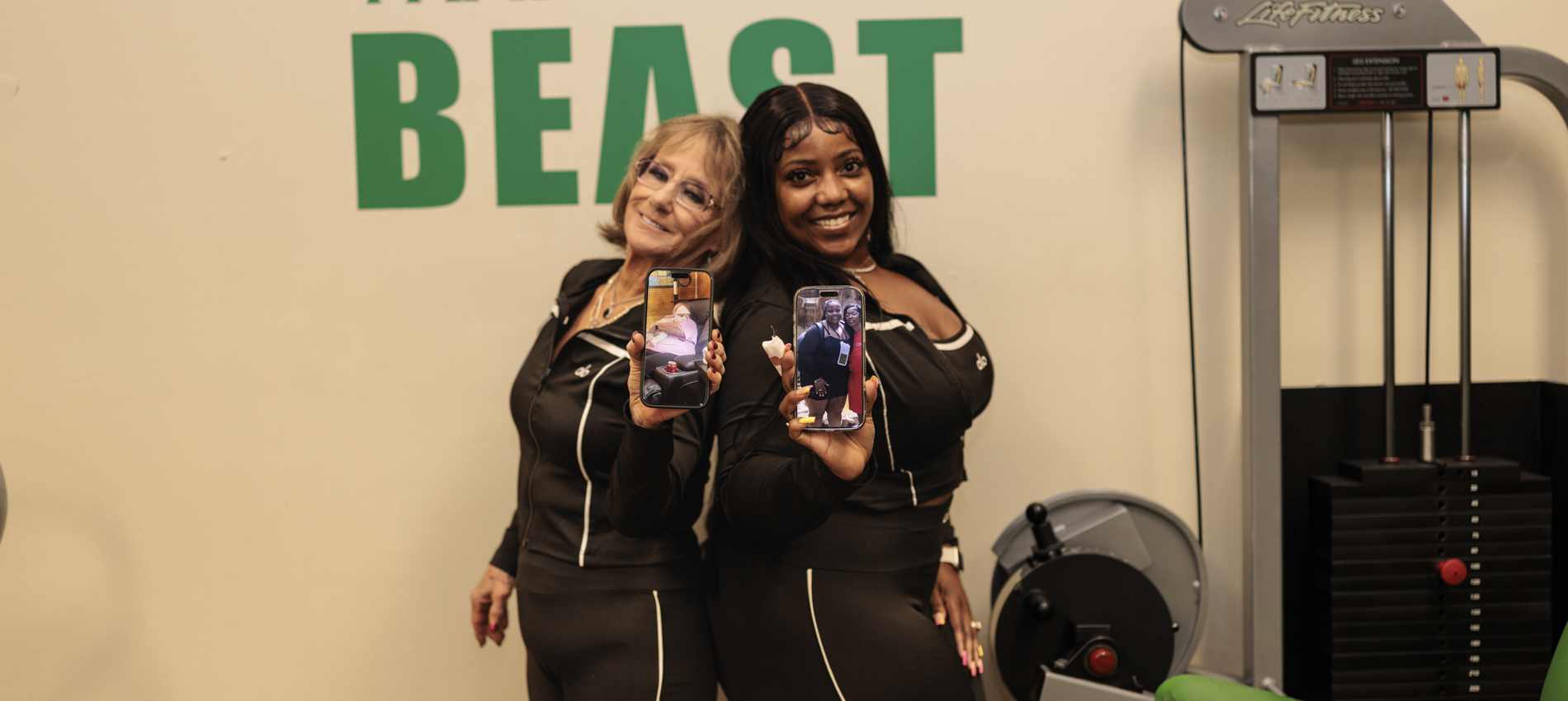 Two women wearing matching workout attire hold out their cell phones, which display photos of each of them before their recent health journeys began.