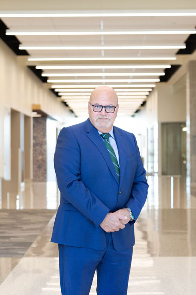 Dr. Taglialatela specializes in Alzheimer’s disease research at UTMB, and serves as the institution’s inaugural Director of the Moody Brain Health Institute. Person in a blue suit and striped tie stands in a modern hallway with polished floors and overhead linear lighting.