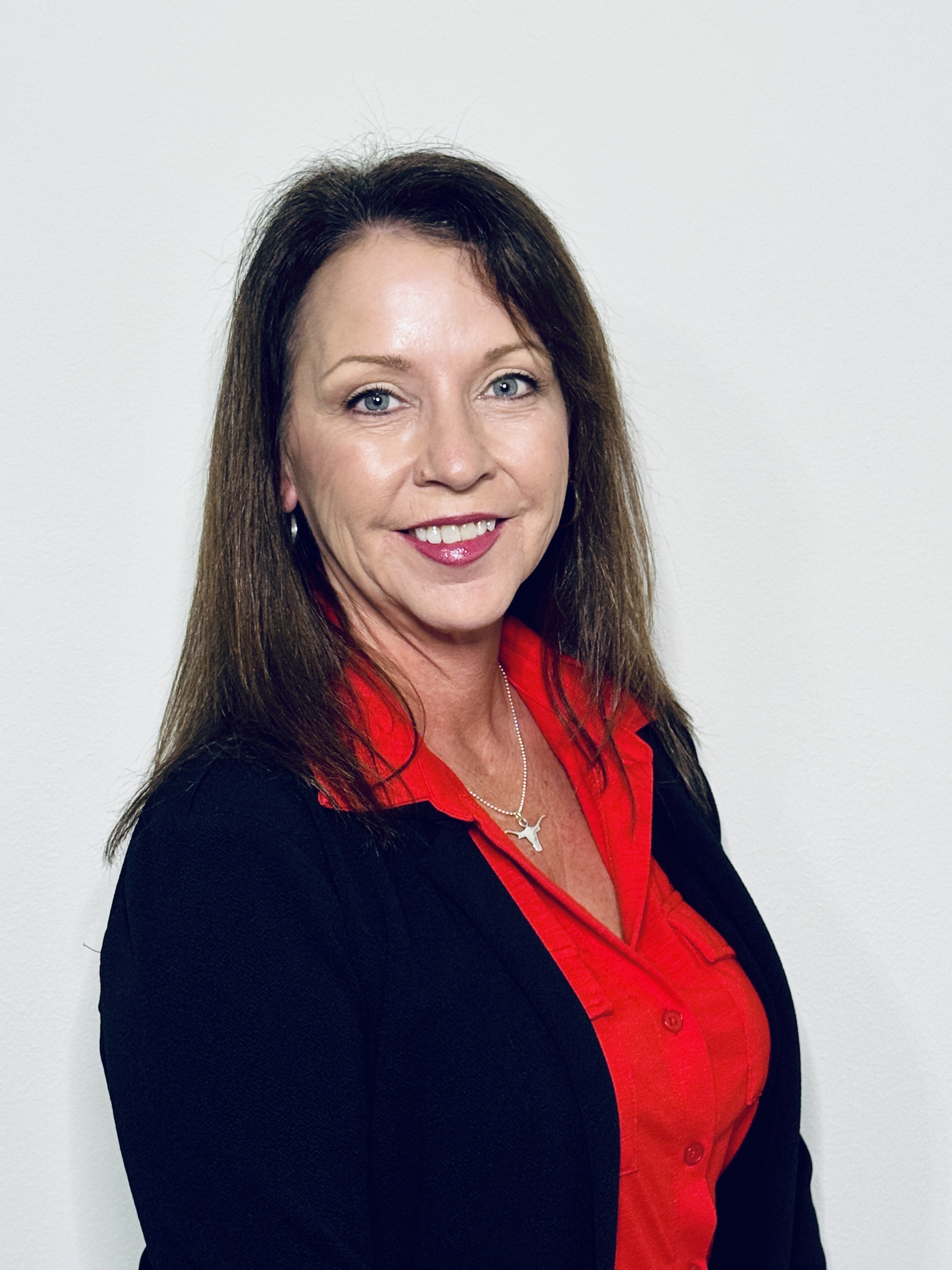 Professional headshot of a woman with long brown hair, red shirt, and blue jacket.