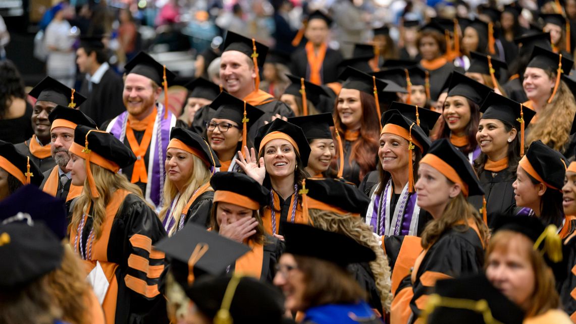 A crowd of UTMB nursing students at graduation dressed in black cap and gowns and orange sashes