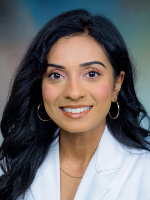 Dr. Neepa Patel Professional headshot shows a woman with dark hair wearing a white coat against a blue-gray background, facing the camera.
