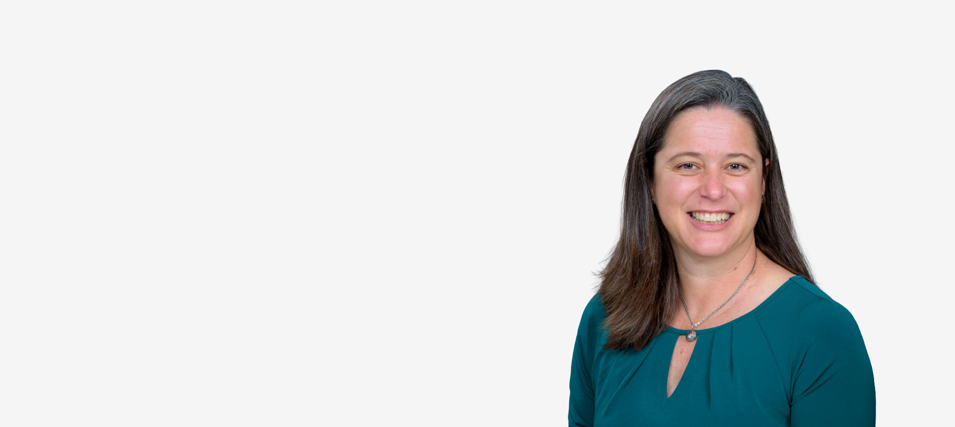 Formal head-and-shoulders studio portrait of a woman with long brown hair wearing a teal top and a necklace against a white background